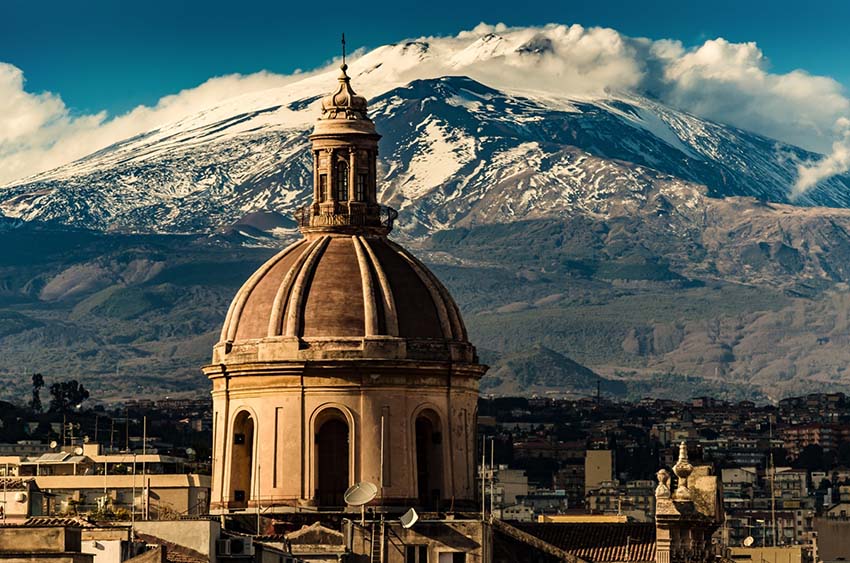 The dome of Cathedral in Catania on the background of volcano Etna in the snow.. The view of the city of Catania with the view of Etna volcano, Sicily, Italy. Catania the UNESCO World Heritage.